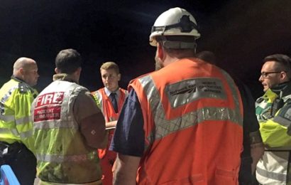 A group of firefighters, police, network rail staff and ambulance crew standing together, some with backs turned, discussing the incident at Burnham railway station at night time