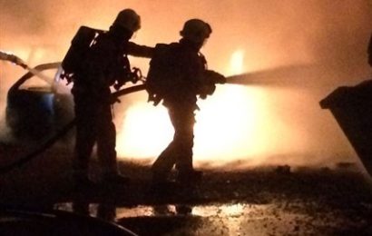 Silhouette of two firefighters in front of flames using a hose reel to extinguish a fire in an incident that destroyed 14 cars in a blaze in Langley