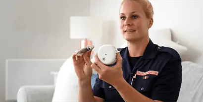 Female firefighter sitting on sofa holding a smoke alarm