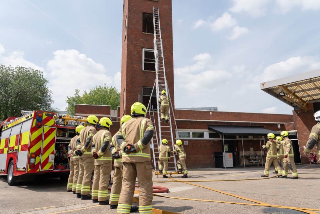 Firefighters doing a ladder rescue drill with a ladder climbing a drill tower.