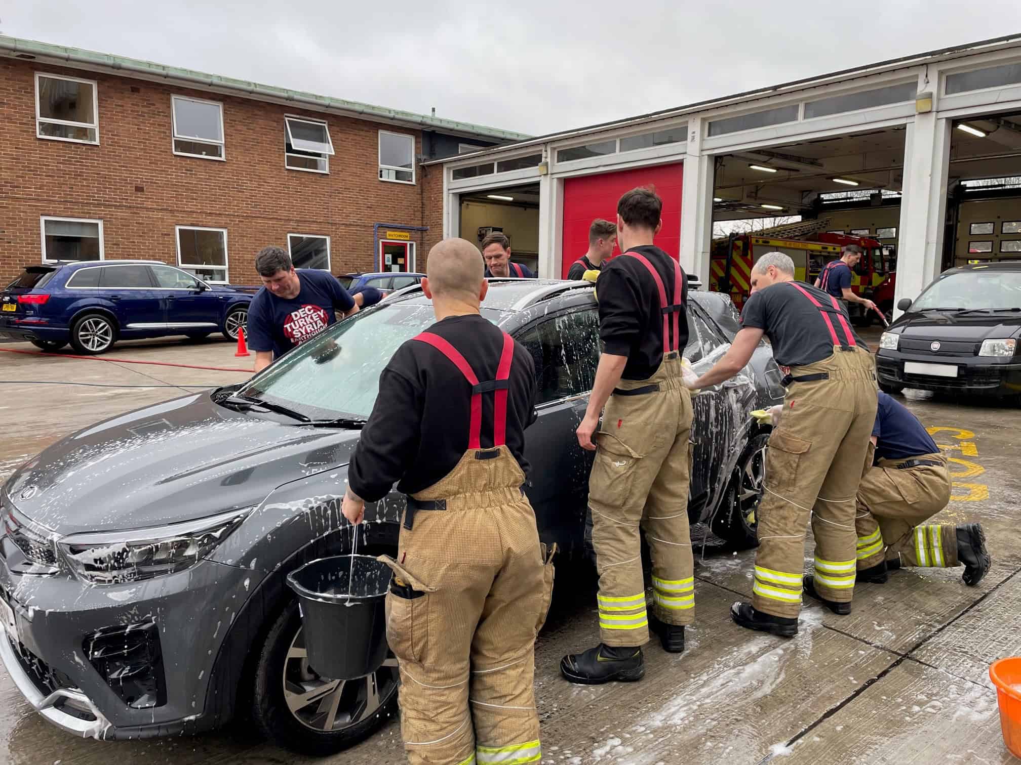 Firefighters at Slough Fire Station washing a car with soapy water and sponges