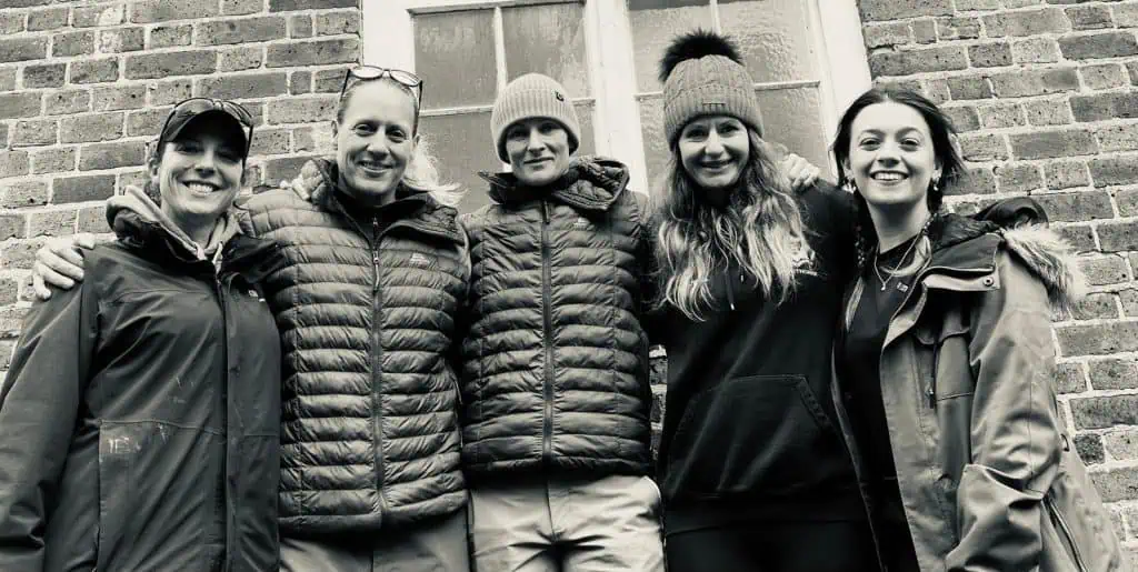 five women smiling while wearing winter coats and hats.