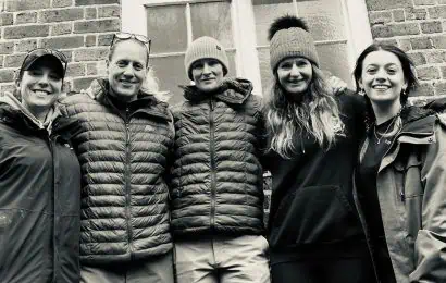 Black and white photo of five women wearing winter puffer coats and hats.